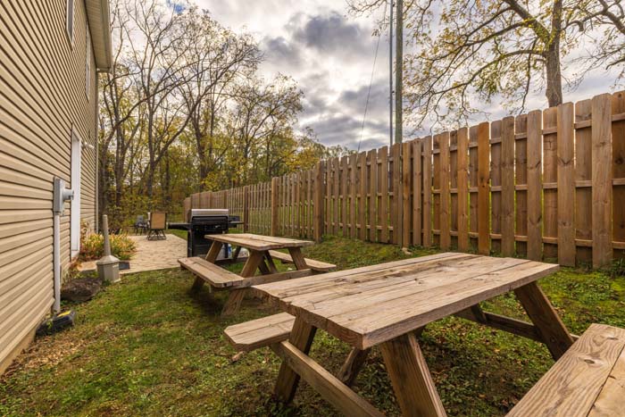 Fenced side yard with two picnic tables and a grill