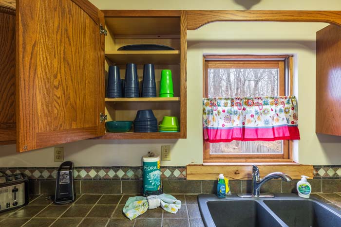 Open cabinet with cups and colorful bowls by the sink