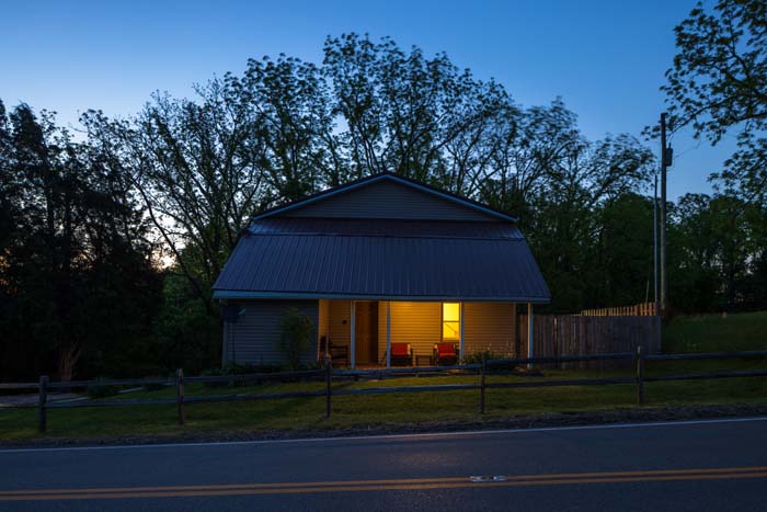 Front exterior at dusk with covered porch and lit seating