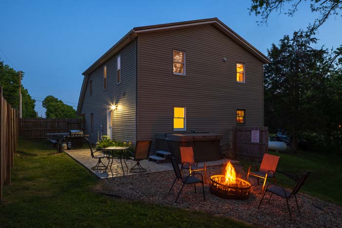 Backyard at dusk with lit fire pit, patio, and hot tub