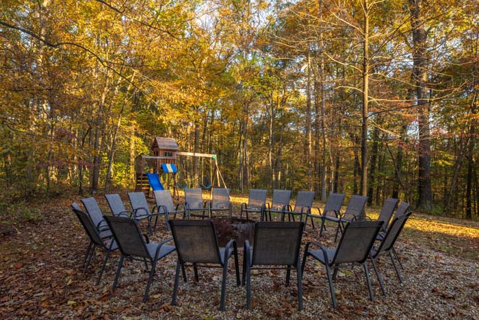 Outdoor fire pit ringed with chairs beside the playground at Peach Tree Lodge