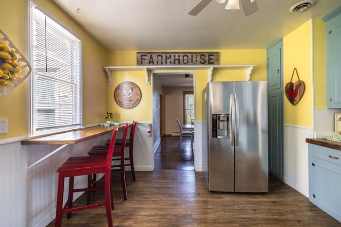 Kitchen with red bar stools, farmhouse sign, and refrigerator