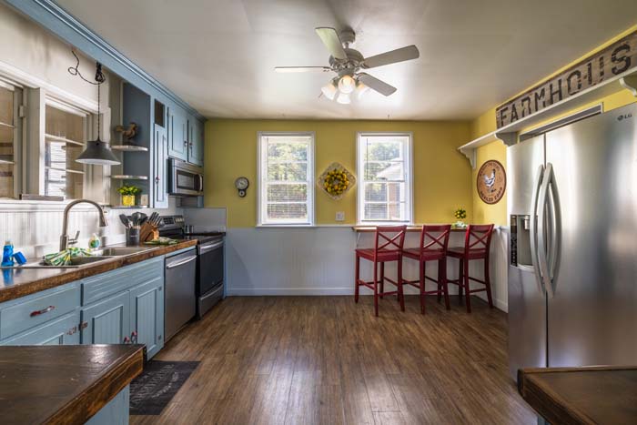 Open farmhouse kitchen with blue cabinets and red stools