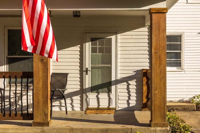 Sunlit covered porch with flag and chairs