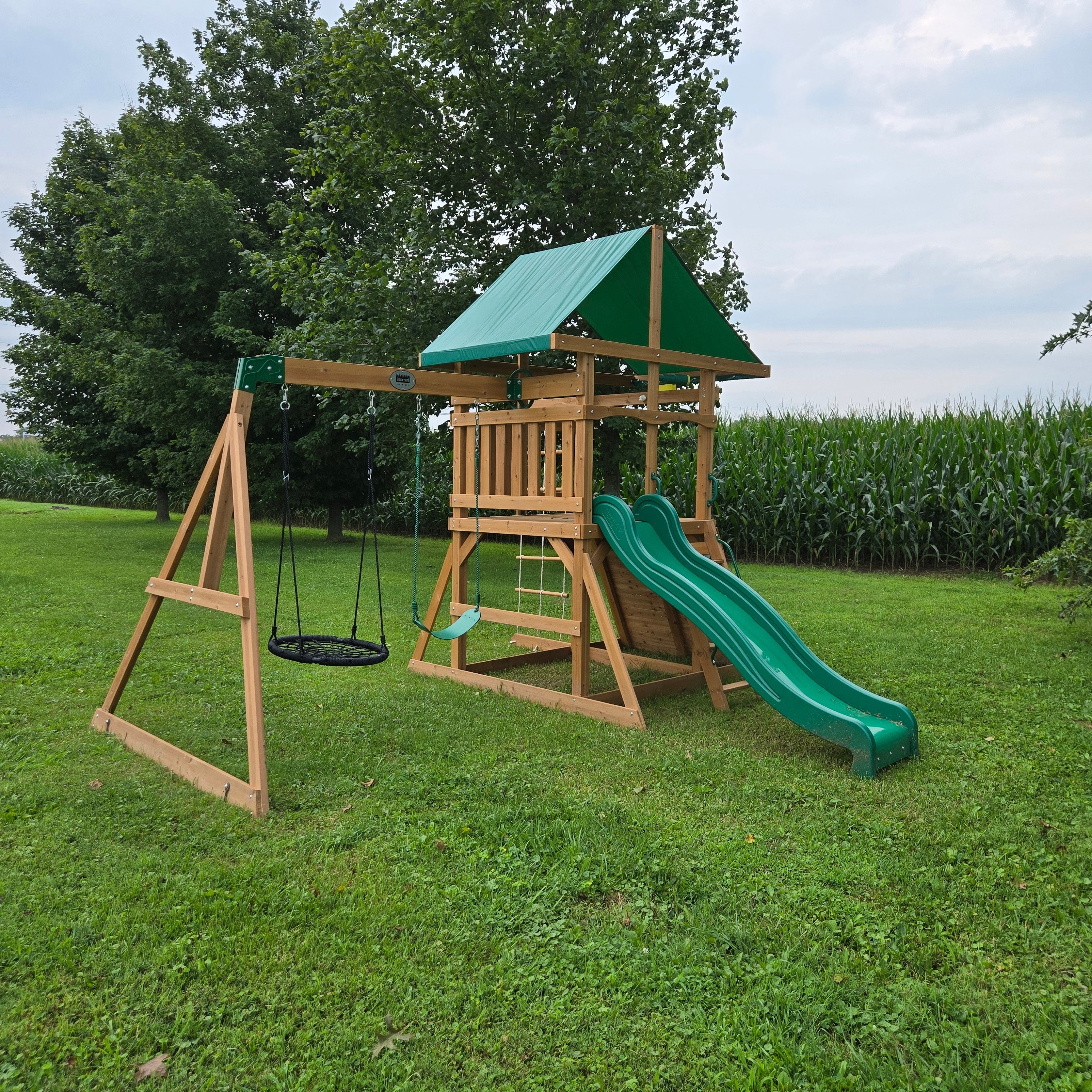 Wooden swing set with green slide, saucer swing and rope ladder on the lawn at Dragonfly Inn