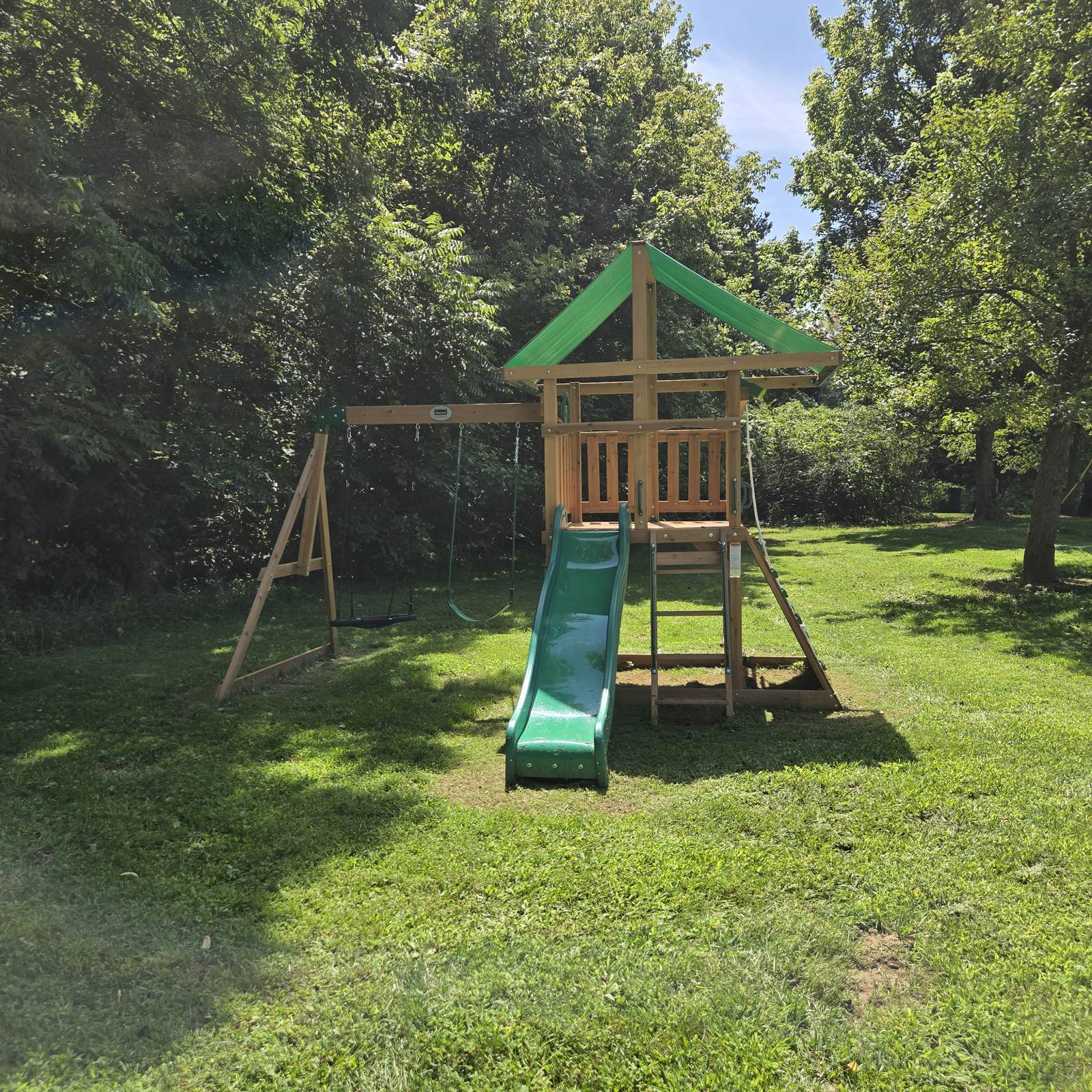 Wooden playset with two swings, a green slide, a climbing wall and a covered fort in the yard at The Hocking Hoot in Hocking Hills Ohio